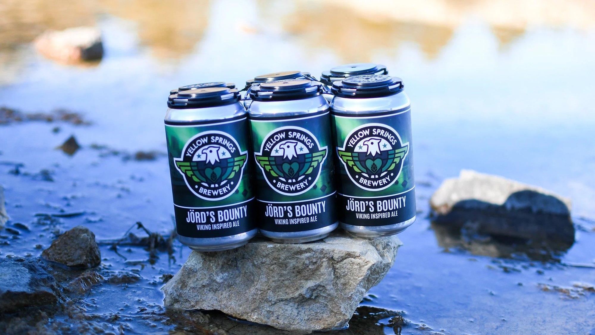 Four cans of Jörd’s Bounty on a rock by the water