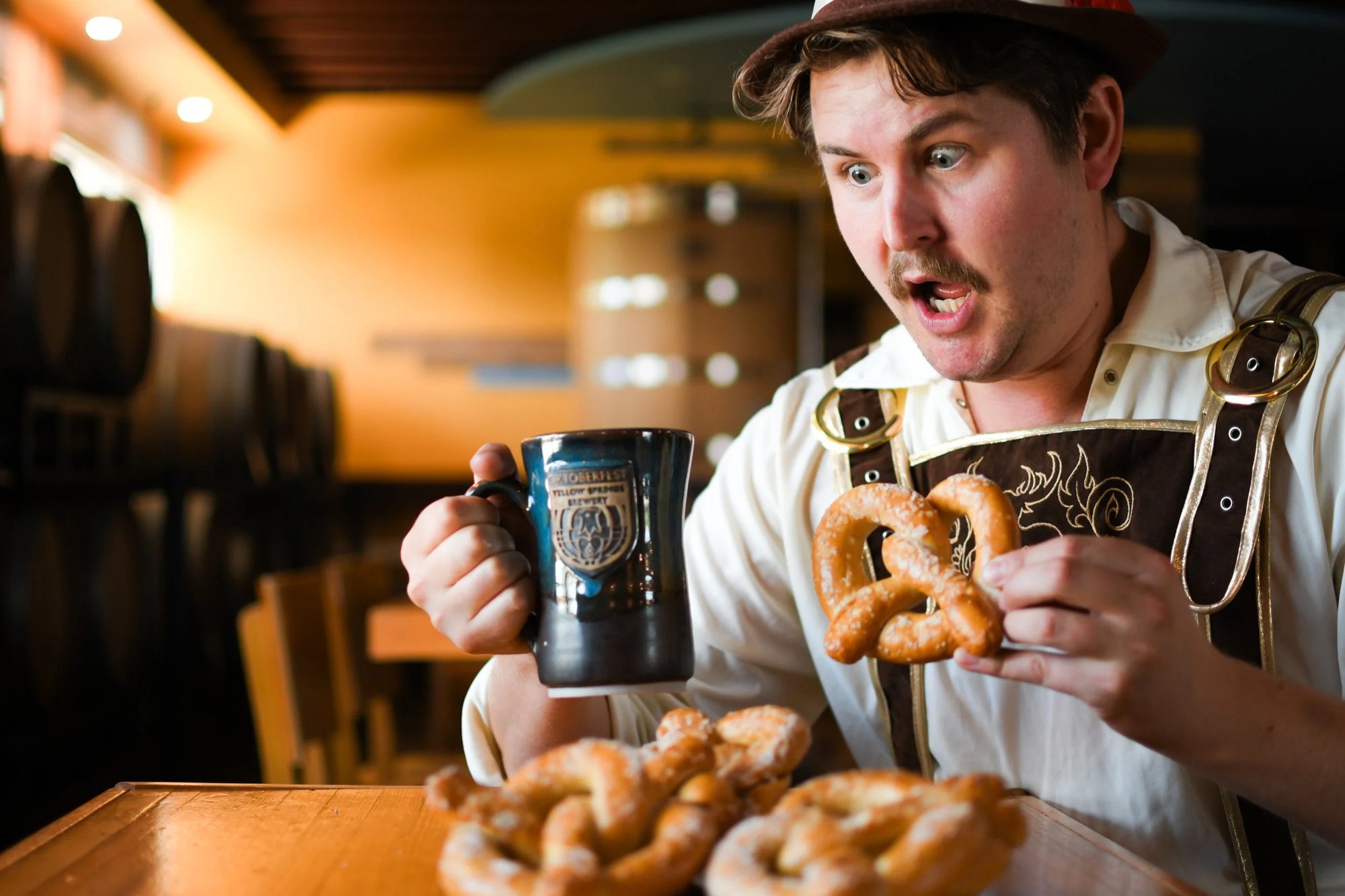 Emcee Elliot Cromer in lederhosen, mid-bite, with a stein and pretzels