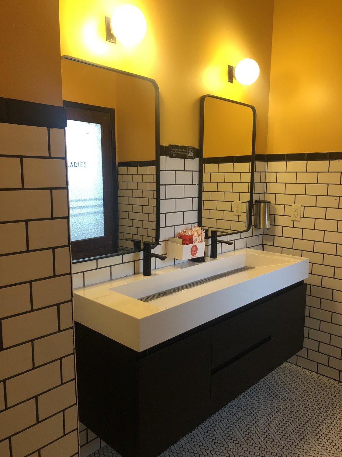 The remodeled restroom: a white trough sink on a black vanity with yellow walls