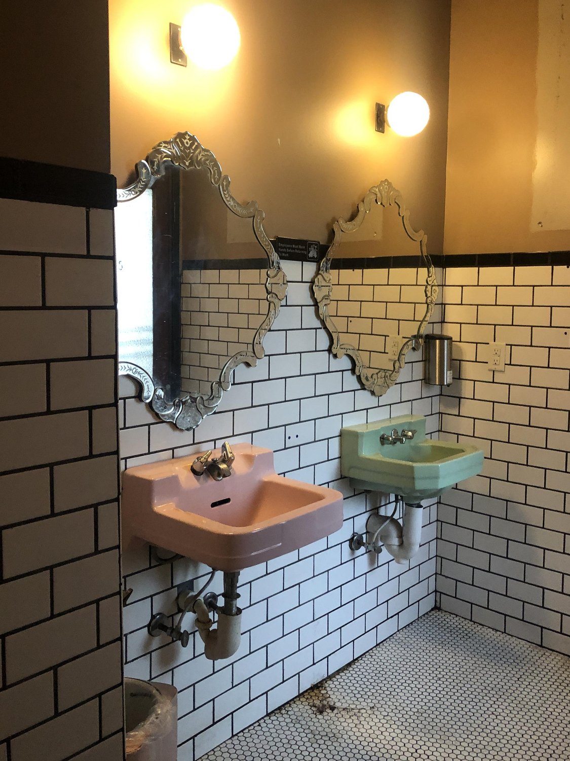 The restroom before the remodel: pink and green sinks under ornate mirrors