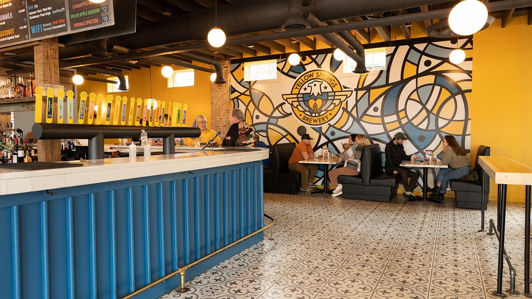 The Columbus taproom: a blue bar, a large brewery mural and guests at the counter